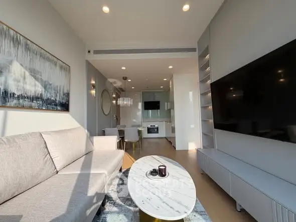 Modern living room with sleek design and large TV, open to dining area and kitchen.