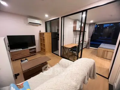 Modern open-layout living room with study area and bedroom, featuring sleek furniture and large glass partitions.