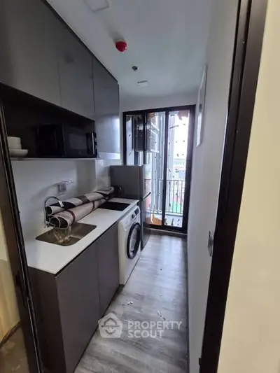 Compact kitchen with modern appliances and washing machine, featuring sleek cabinetry and balcony access.