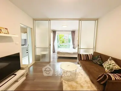 Modern living room with cozy sofa and view into stylish bedroom through glass doors.