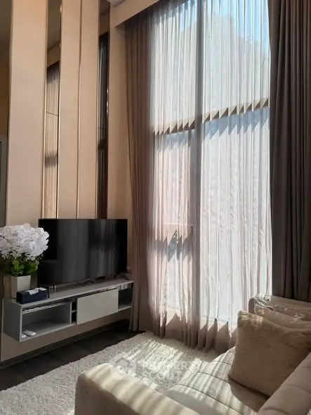 Luxurious living room with high ceilings and elegant decor, featuring a large window with sheer curtains.