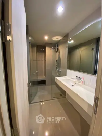 Modern bathroom with glass shower and sleek vanity in contemporary apartment.