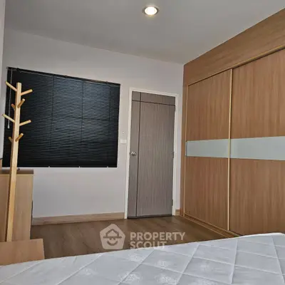 Modern bedroom with wooden flooring and built-in wardrobe, featuring sleek blinds and cozy ambiance.