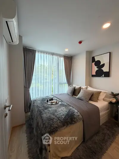 Cozy bedroom with modern decor and large window offering natural light.