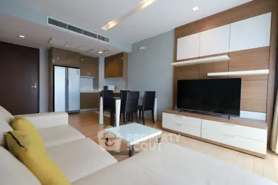 Modern living room with open kitchen, sleek furniture, and large TV in a stylish apartment.