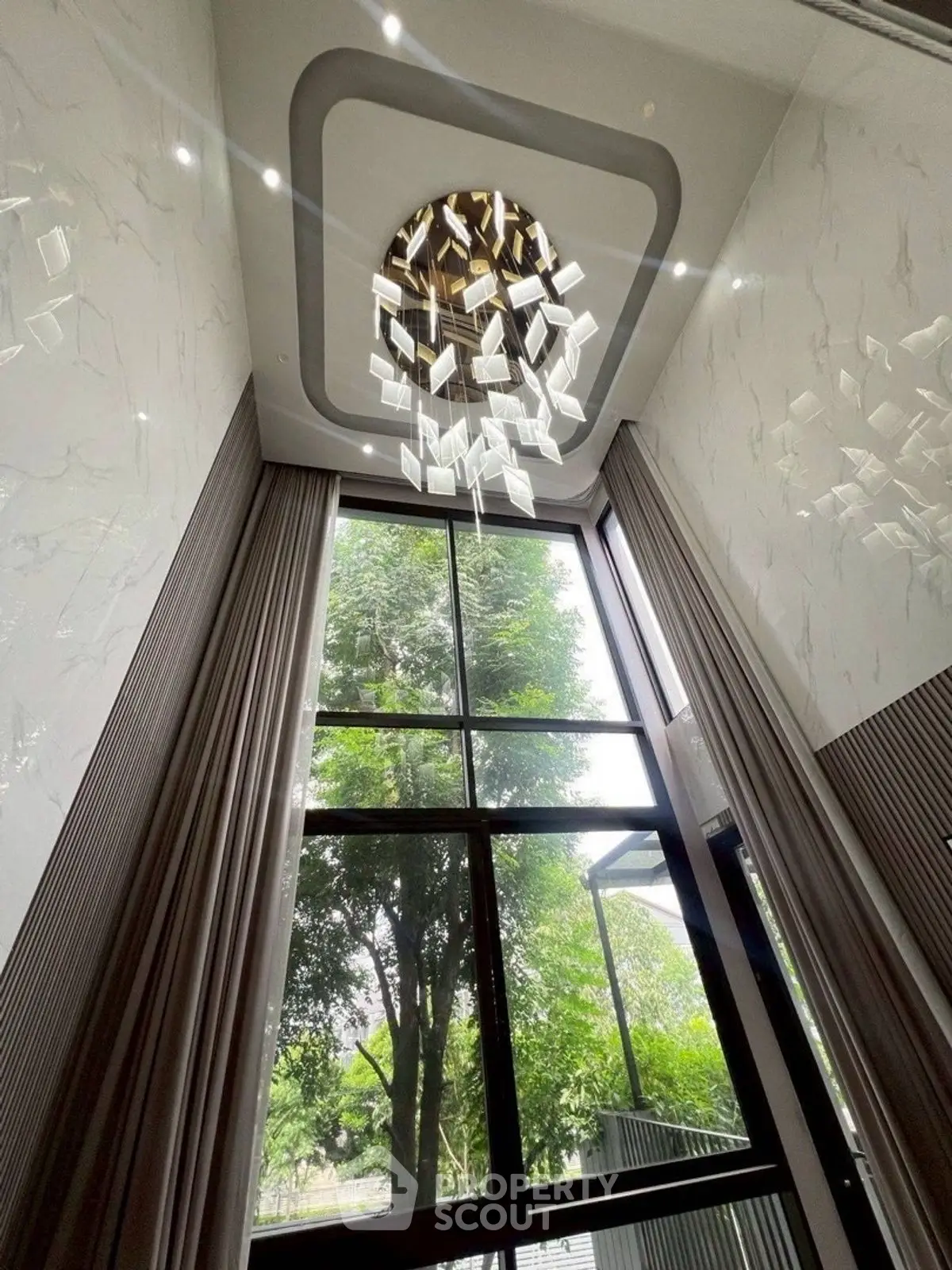 Luxurious high-ceiling living room with stunning chandelier and large windows overlooking greenery.