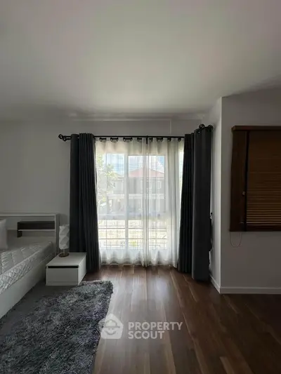 Spacious bedroom with large window and elegant curtains, featuring modern decor and hardwood flooring.