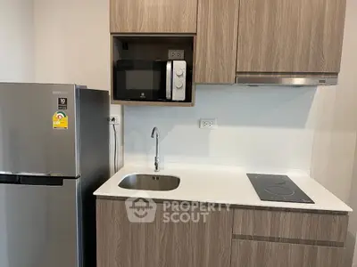 Modern kitchen with sleek appliances and wooden cabinetry, featuring a fridge, microwave, and electric cooktop.