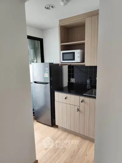 Modern compact kitchen with sleek cabinetry and stainless steel fridge in a cozy apartment.