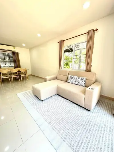 Spacious living room with modern beige sofa and dining area, featuring large windows and natural light.