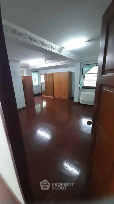 Spacious bedroom with wooden flooring and ample natural light, featuring large wardrobes and elegant ceiling design.
