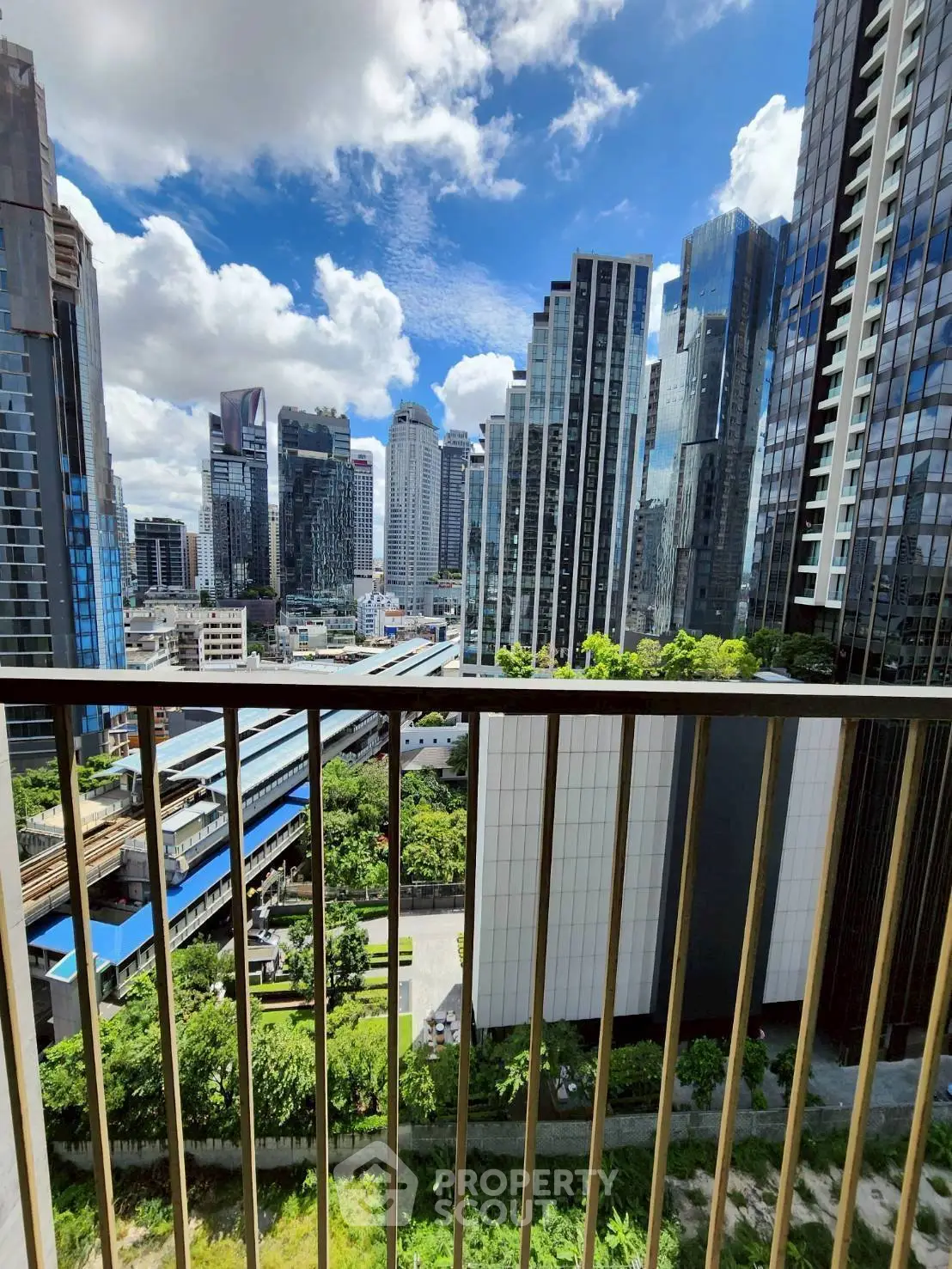 Stunning cityscape view from a high-rise balcony overlooking modern skyscrapers and lush greenery.