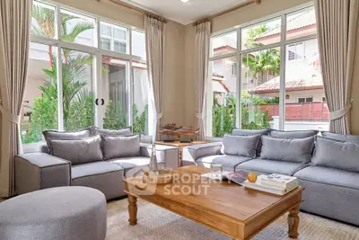 Spacious living room with large windows, cozy gray sofas, and a wooden coffee table in a bright, airy setting.
