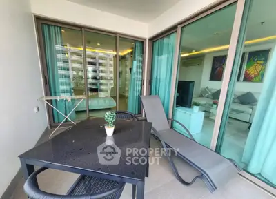 Spacious balcony with modern furniture and glass doors leading to a stylish living room.