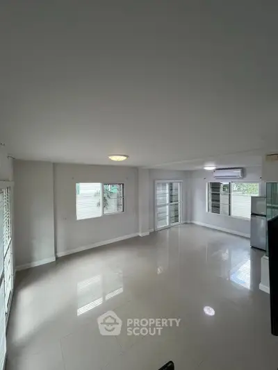 Spacious living room with large windows and glossy tiled floors, perfect for natural light.