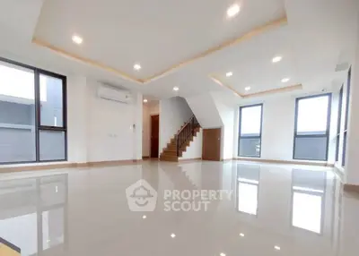 Spacious modern living room with large windows and staircase, featuring sleek tile flooring and recessed lighting.
