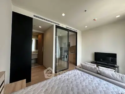 Modern bedroom with open layout, featuring a cozy bed, TV, and a glimpse of the kitchen area.