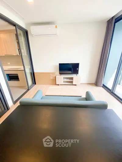 Modern living room with open kitchen and balcony view, featuring sleek furniture and natural light.