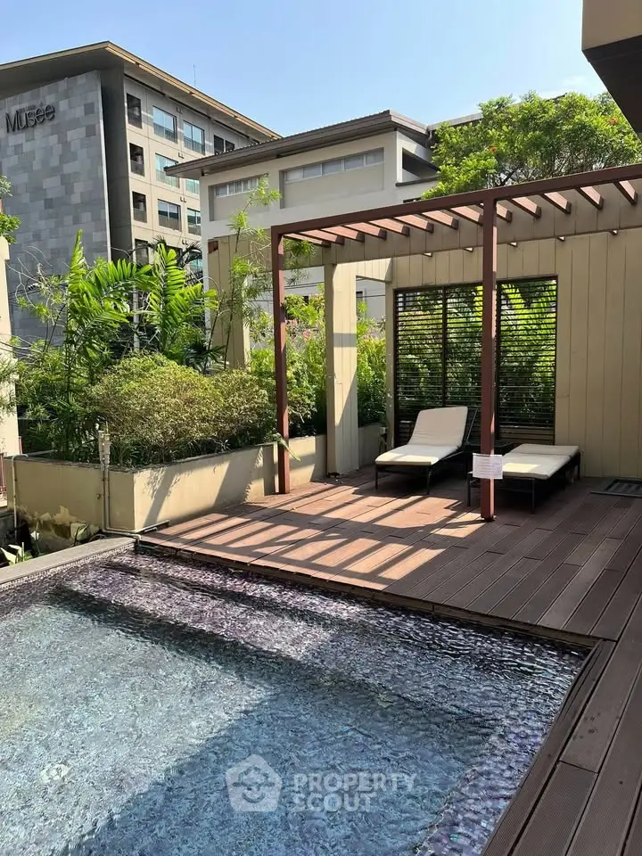Luxurious rooftop pool with sun loungers and pergola, surrounded by lush greenery and modern architecture.