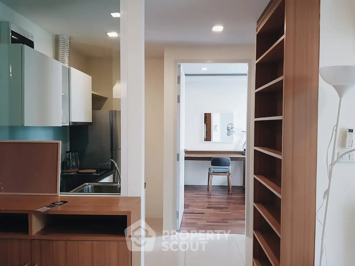 Modern apartment interior with open kitchen and study area, featuring sleek cabinetry and wooden flooring.