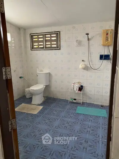 Spacious bathroom with tiled walls and floor, featuring a toilet and shower area.