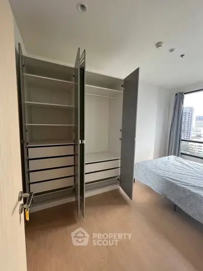 Modern bedroom with open wardrobe and city view window, showcasing sleek design and ample storage space.