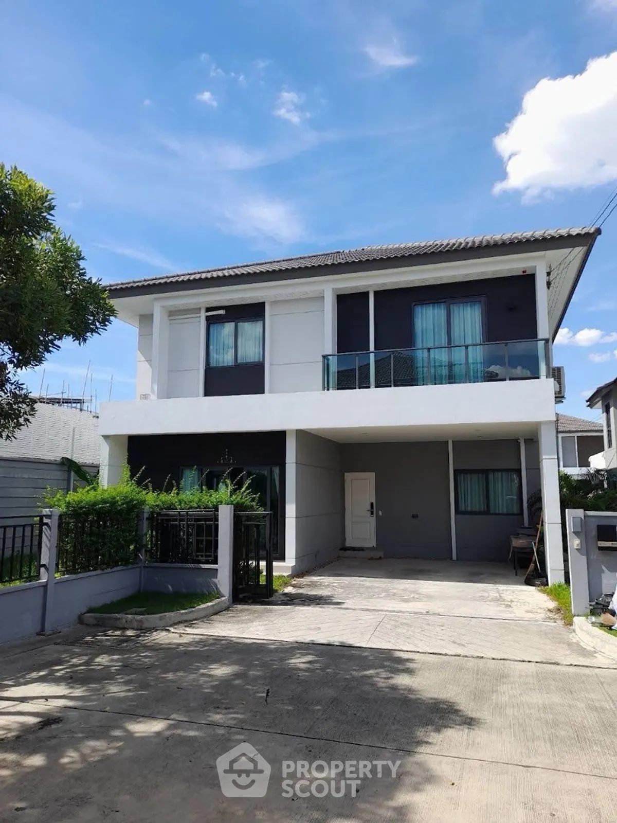Modern two-story house with spacious driveway and lush greenery under a clear blue sky.