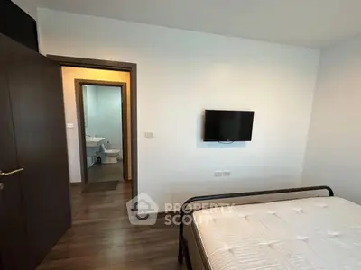 Modern bedroom with wall-mounted TV and view into bathroom, featuring sleek wooden flooring.