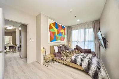 Modern bedroom with colorful art, cozy bed, and large window in stylish apartment.
