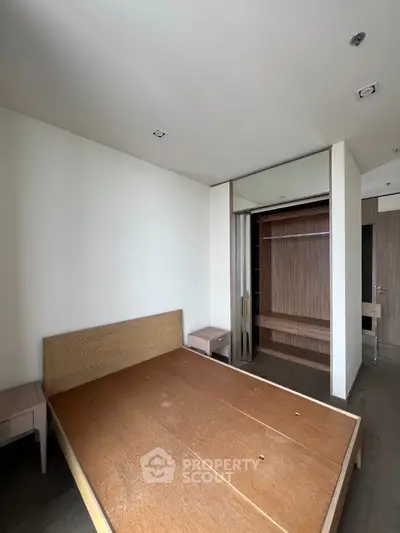 Spacious bedroom with wooden bed frame and built-in closet in modern apartment.