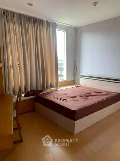 Cozy bedroom with large window and wooden flooring, perfect for relaxation.