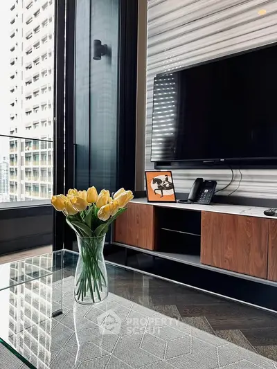 Modern living room with glass table, TV, and city view from balcony.