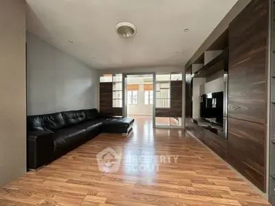 Spacious modern living room with sleek wooden flooring and stylish black leather sofa.