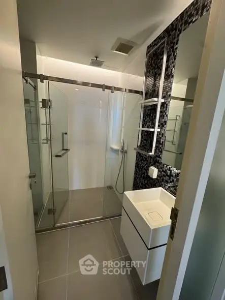 Modern bathroom with glass shower enclosure and sleek vanity in contemporary apartment.