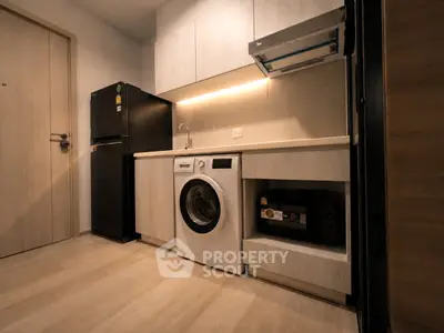 Modern kitchen with sleek appliances and wooden cabinetry, featuring a washing machine and refrigerator.