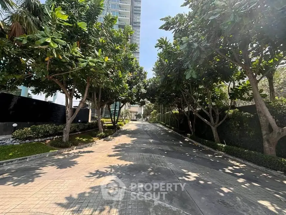 Lush garden pathway leading to a modern high-rise building entrance.