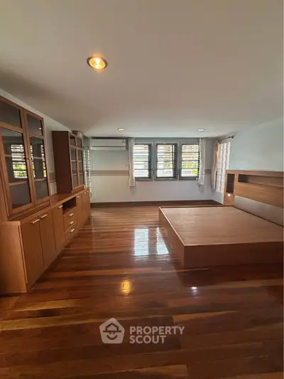 Spacious bedroom with wooden flooring and built-in storage, featuring large windows for natural light.