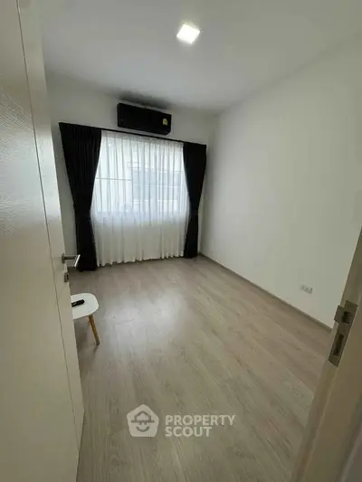 Spacious empty room with wooden flooring and large window, perfect for customization.