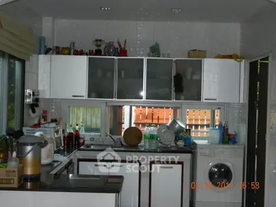 Modern kitchen with sleek cabinets and washing machine, featuring ample natural light and functional layout.