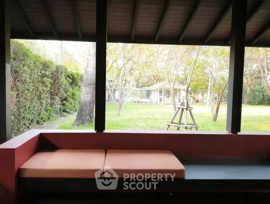 Charming outdoor view from a covered patio with comfortable seating, overlooking a lush garden and distant house.
