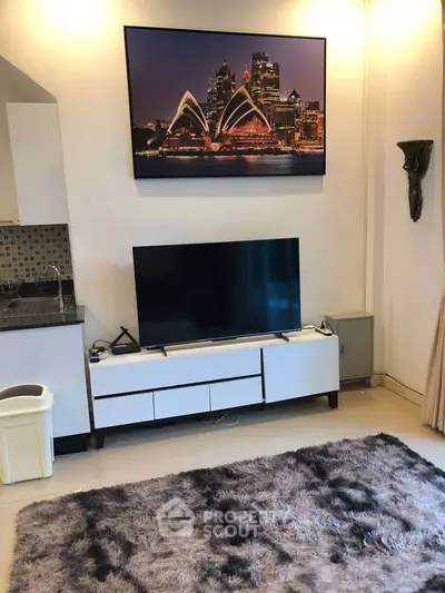 Modern living room with stylish decor and large TV, featuring a cozy rug and contemporary artwork.