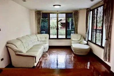 Spacious living room with white leather sofa and large windows offering garden view.