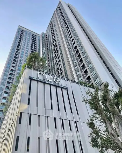 Modern high-rise building with sleek design and lush greenery in urban setting.