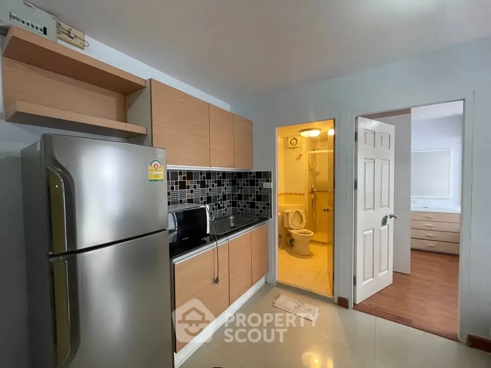 Modern compact kitchen with stainless steel fridge and adjacent bathroom in cozy apartment.