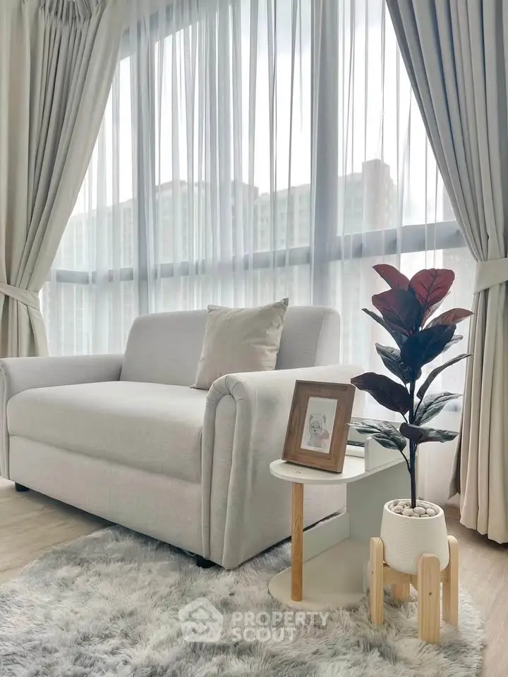 Elegant living room with cozy sofa, stylish side table, and lush plant, featuring floor-to-ceiling windows and soft curtains.