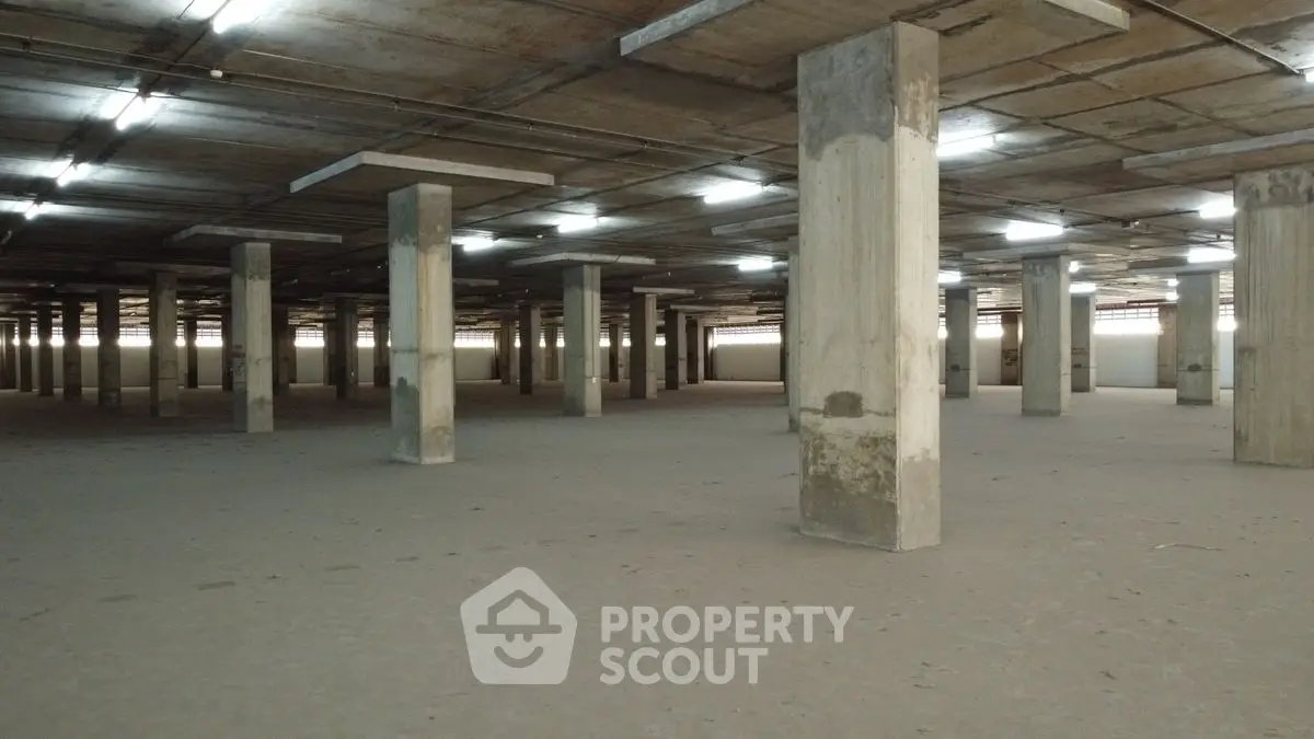 Spacious industrial warehouse with concrete pillars and high ceilings, ideal for storage or manufacturing.