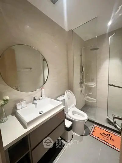 Modern bathroom with glass shower, round mirror, and sleek vanity in luxury apartment.