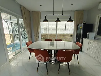 Elegant dining area with marble table and red chairs, overlooking a pool through large windows.