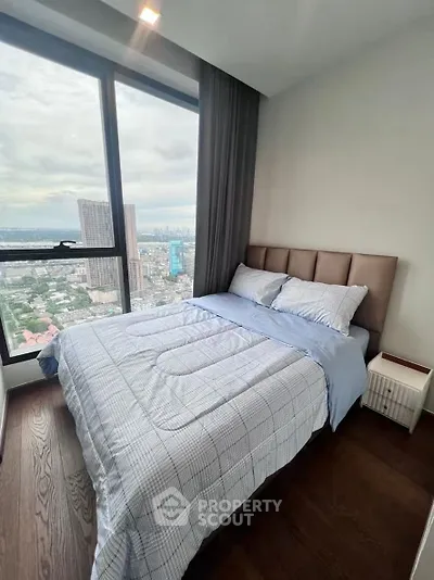 Cozy bedroom with stunning city view from large window, featuring modern decor and plush bedding.
