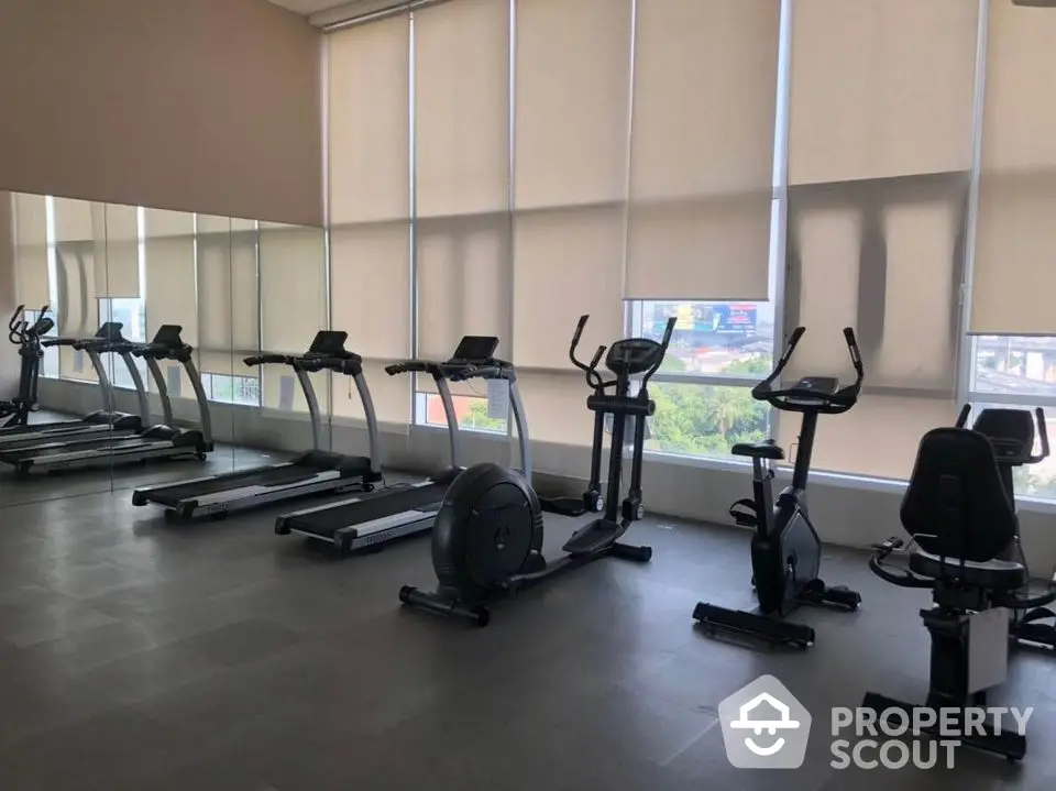 Modern gym with exercise equipment and large windows in upscale residential building.